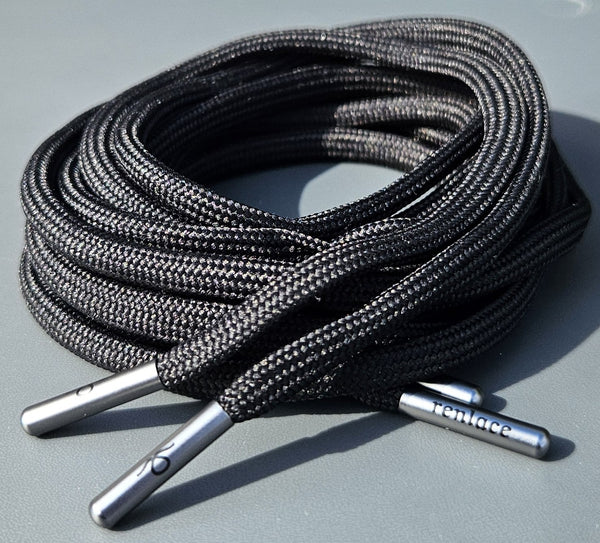 Coiled black shoelaces with silver metal tips on a gray surface