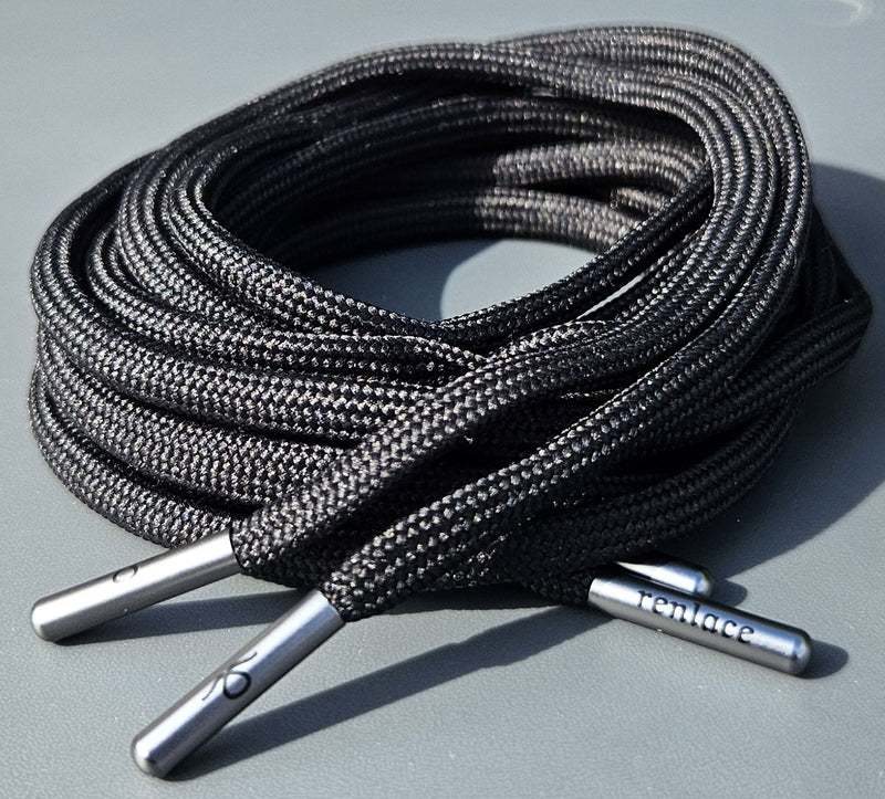 Coiled black shoelaces with silver metal tips on a gray surfaceN°01 Slim Trainer Lace in Black // Gun Metal