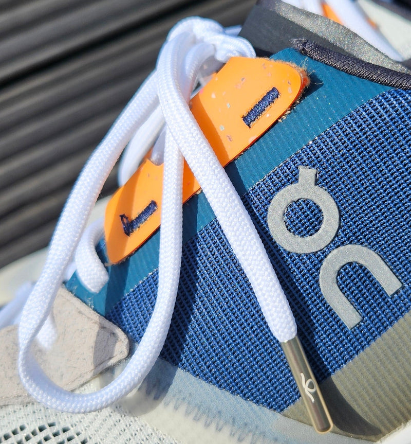 Close-up of a shoe with a blue strap and 'oc' branding on a wooden surfaceN°01 Slim Trainer Lace in Black // Gun Metal
